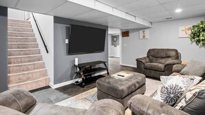 Un salon moderne doté d’un téléviseur à écran plat, de sièges confortables, d’un escalier et d’un jeu de fléchettes.
