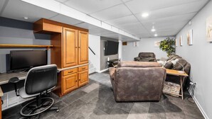 Un bureau moderne, aménagé dans un espace de la maison, avec un bureau, un ordinateur et un fauteuil en cuir. On aperçoit, à l’arrière-plan, une grande armoire avec des tiroirs et un téléviseur.