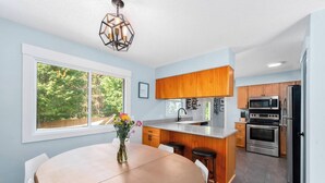 Une cuisine moderne dotée d’un îlot central, de meubles en bois, d’appareils électroménagers en acier inoxydable et d’une grande fenêtre offrant une vue sur la verdure.