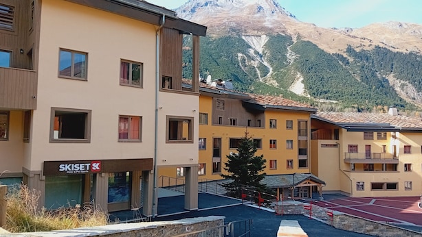 Een meerlaags hotel met een bord van een skigebied, stenen trappen en een berg op de achtergrond.