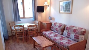 Een gezellige kamer met een houten bank, een klein tafeltje en een eettafel met stoelen.