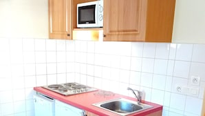 Een kleine keuken met houten kastjes, een ingebouwde magnetron, een vaatwasser en een spoelbak.