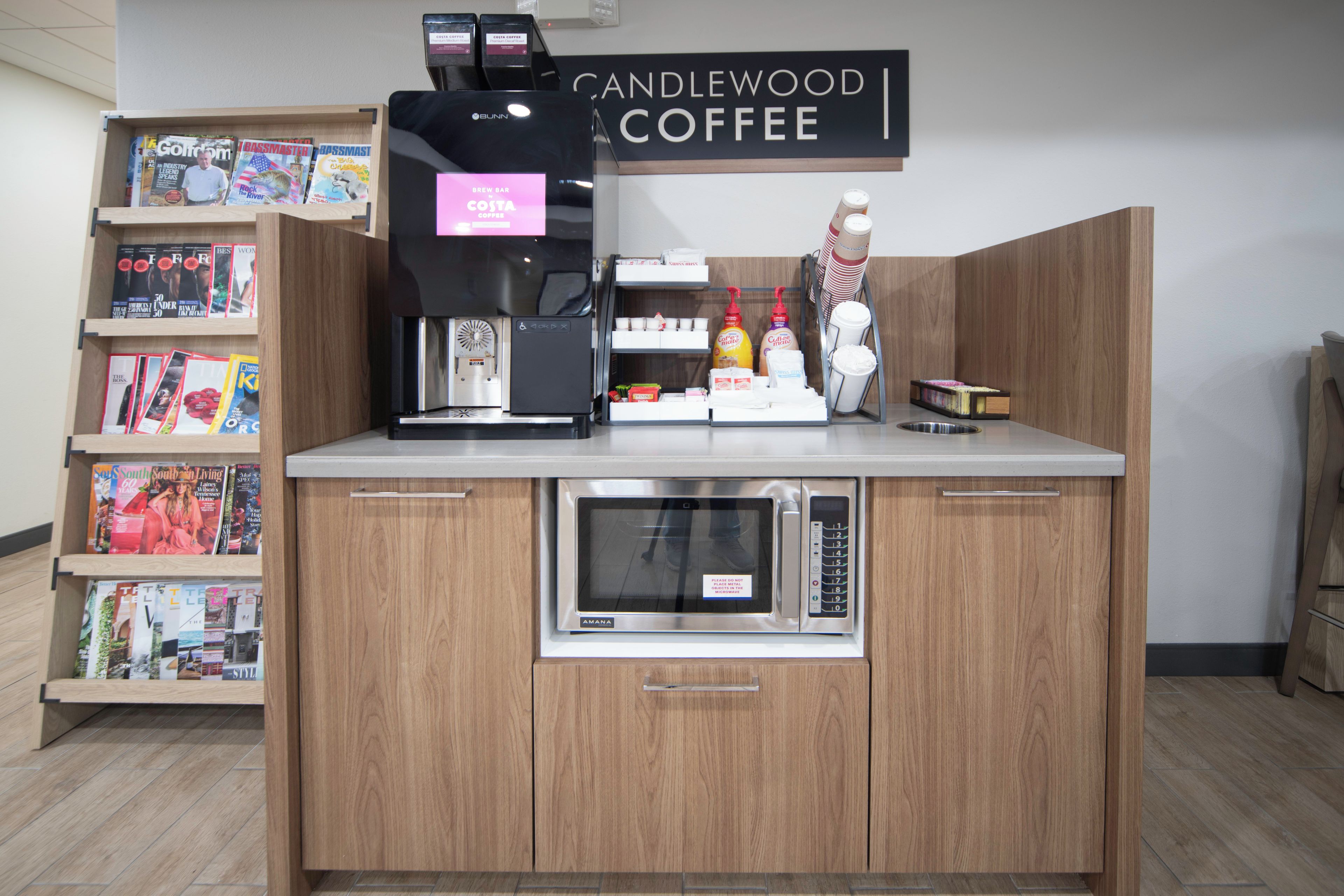 En kaffestation med en kaffemaskin, kaffekoppar och en skylt med texten ”Candlewood Coffee”.