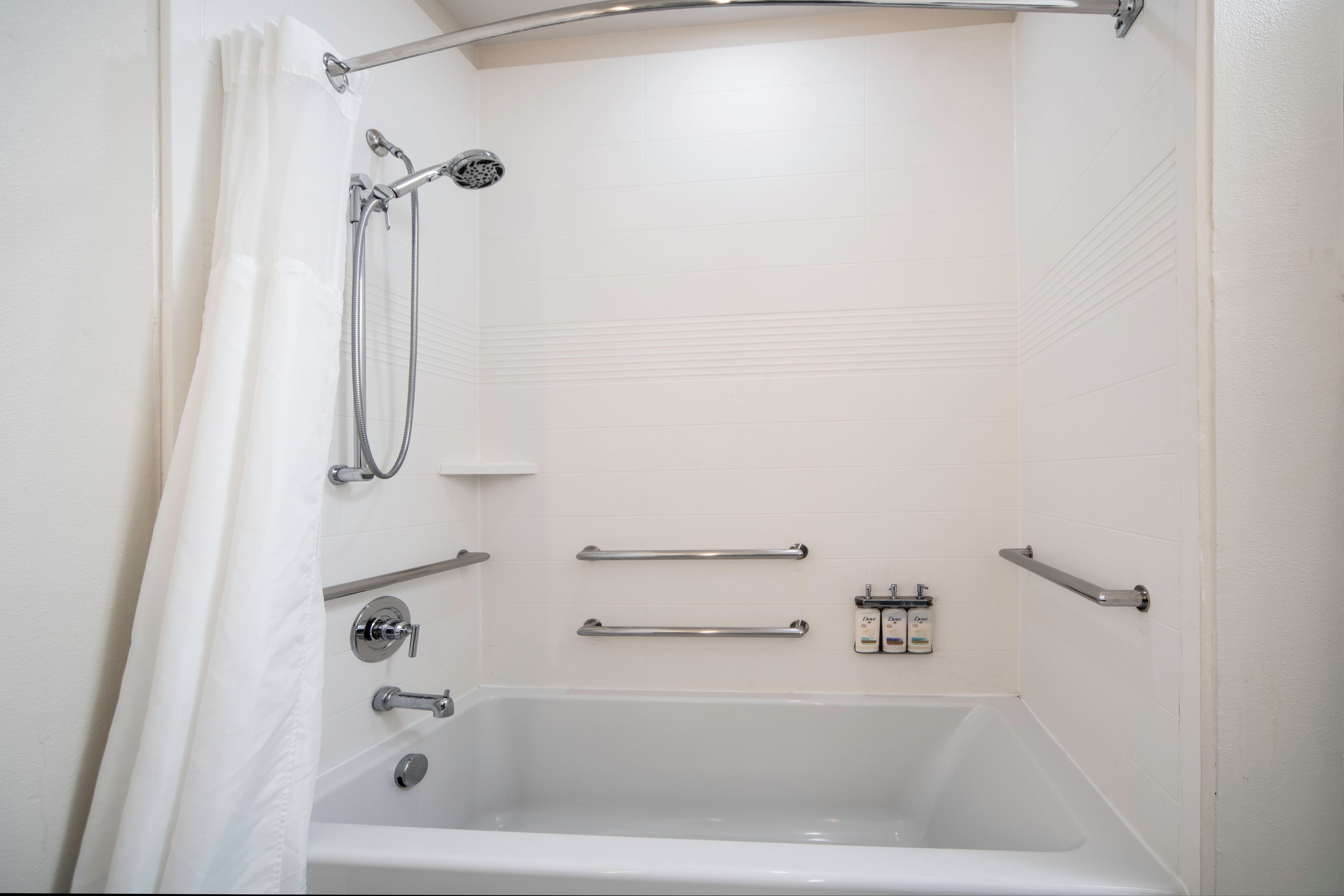 Een witte badkamer met een bad, douche en handgrepen.