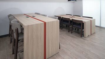 Un salón de conferencias con una larga mesa, sillas y dos lámparas colgantes.