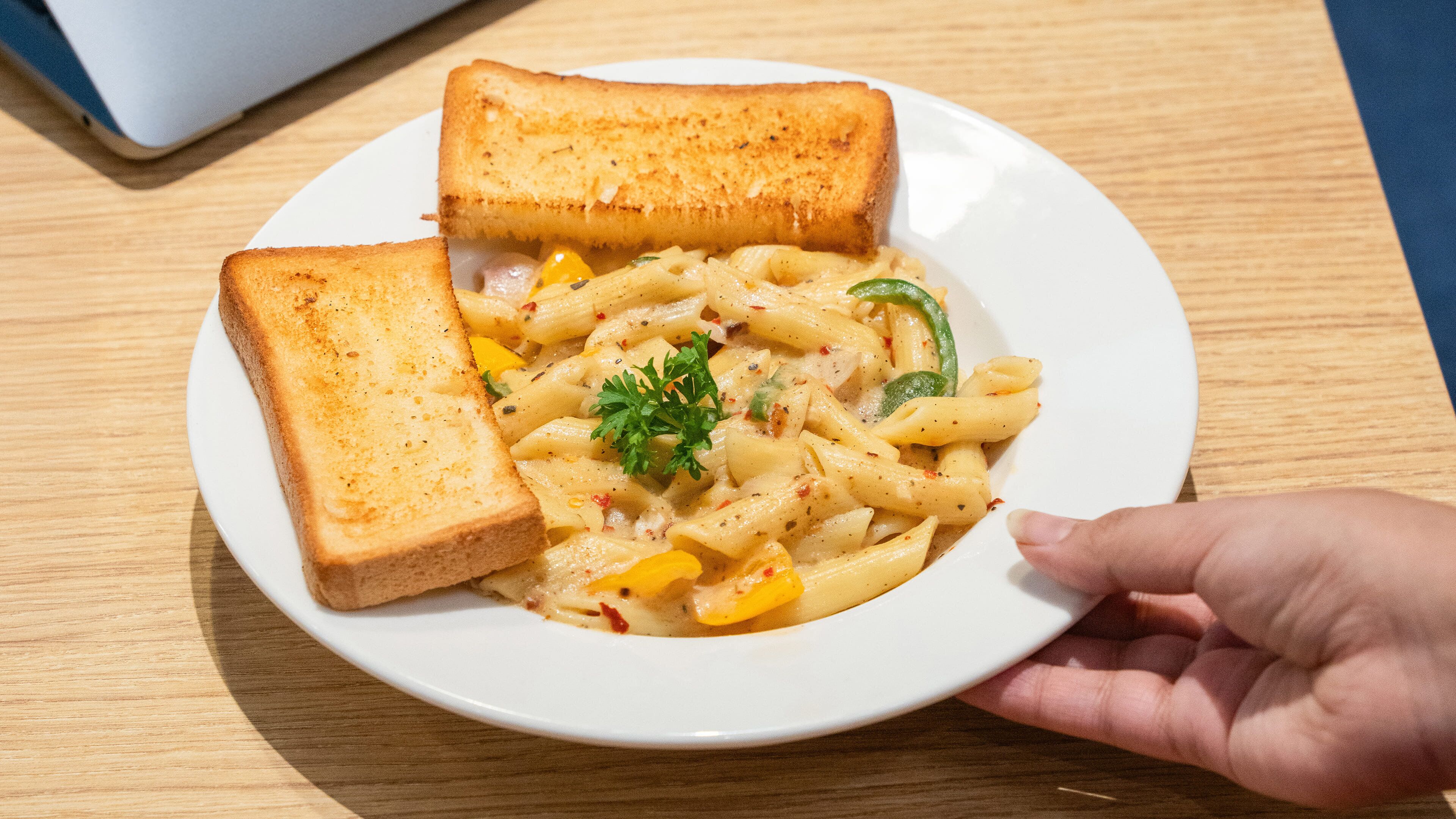 A plate of pasta with two slices of toasted bread and a garnish, held by a hand.