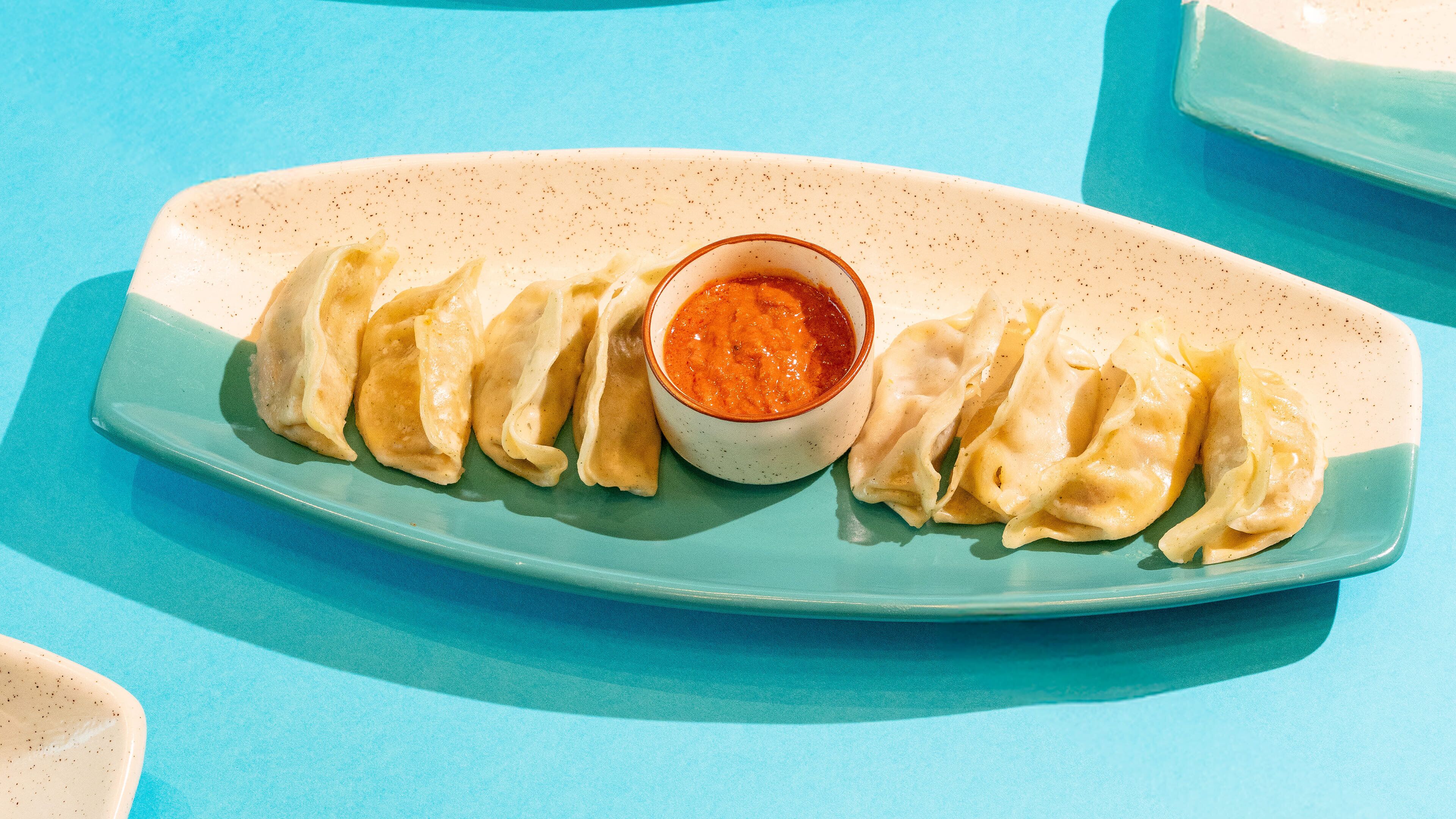A plate of dumplings with a dipping sauce on a blue plate.