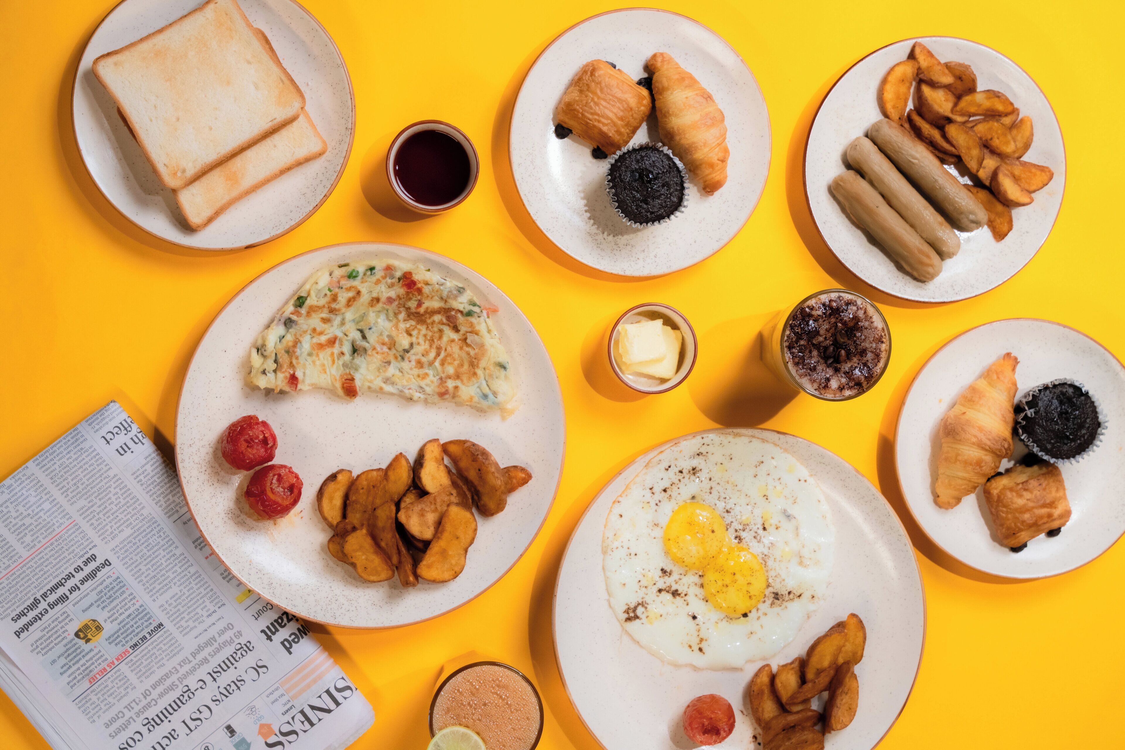 A breakfast spread on a yellow table with toast, croissants, eggs, and various pastries.
