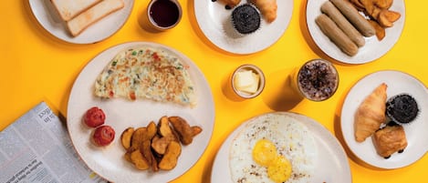 A breakfast spread on a yellow table with toast, croissants, eggs, and various pastries.