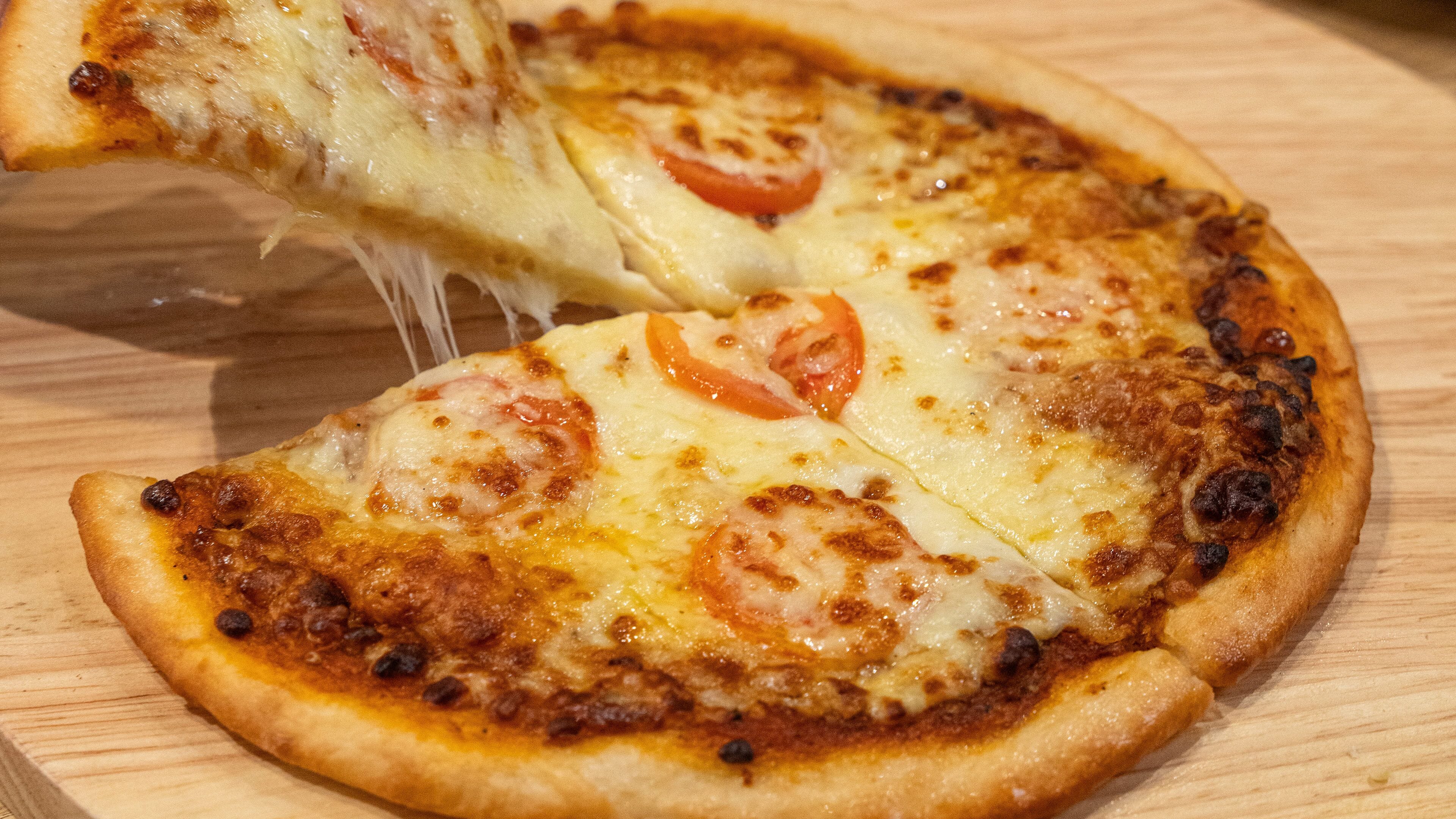 A pizza with cheese and tomato slices on a wooden surface.