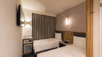 Ein Hotelzimmer mit zwei Betten, einem Flachbildfernseher, einem Nachttisch mit Telefon, einer Lampe und einem an der Wand befestigten Spiegel.