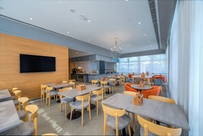 A modern dining area with multiple tables and chairs, a flat-screen TV mounted on the wall, and a kitchen area in the background. - Holiday Inn Express Kolkata New Town by IHG (Barasat)