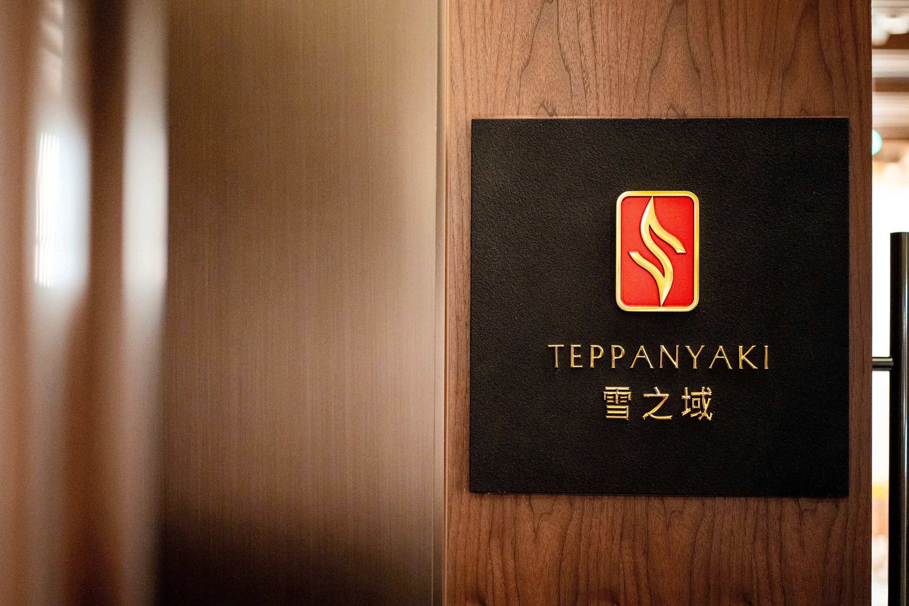 A black sign with gold lettering and a red logo on a wooden door.