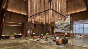 A spacious lobby with a high ceiling, wooden paneling, a central seating area with sofas and tables, and a large mural depicting a mountainous landscape. - Shanghai Snow World Hotel, Vignette Collection by IHG (Shanghai)
