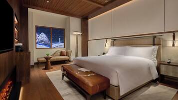 A modern bedroom with a large bed, a bench, a sofa, and a fireplace.