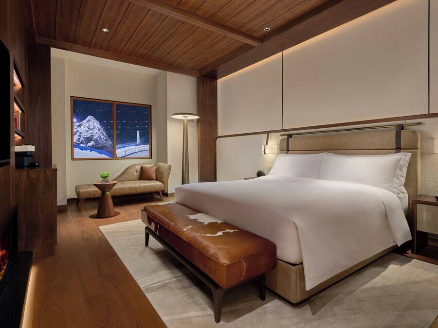 A modern bedroom with a large bed, a bench, a sofa, and a fireplace.