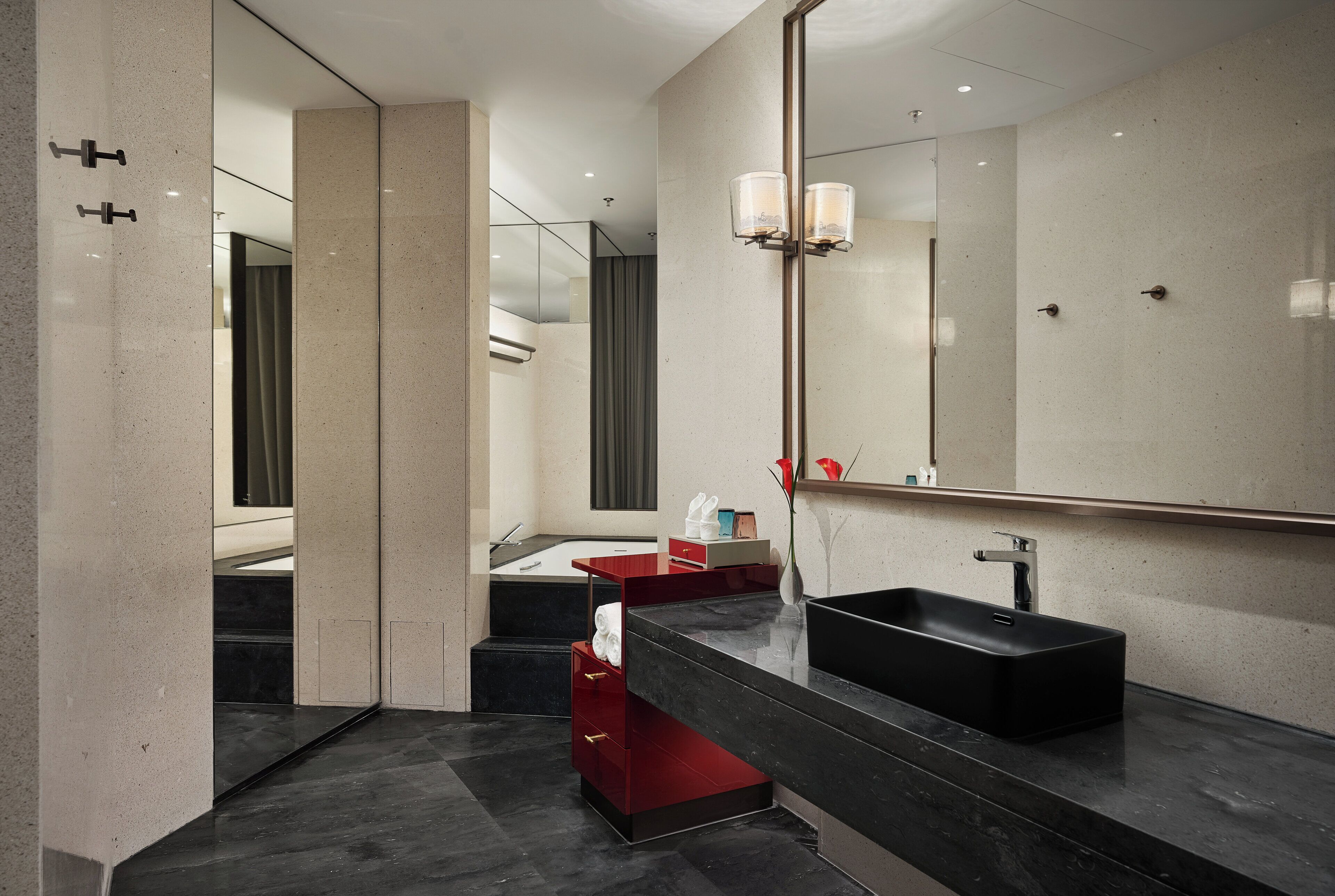 A modern bathroom with a black sink, a large mirror, and a red storage unit.