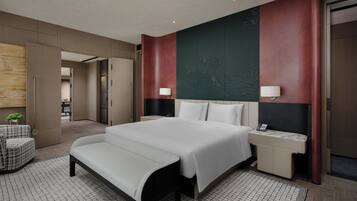 A modern hotel room with a large bed, bedside tables, a bench, and a view of the hallway.