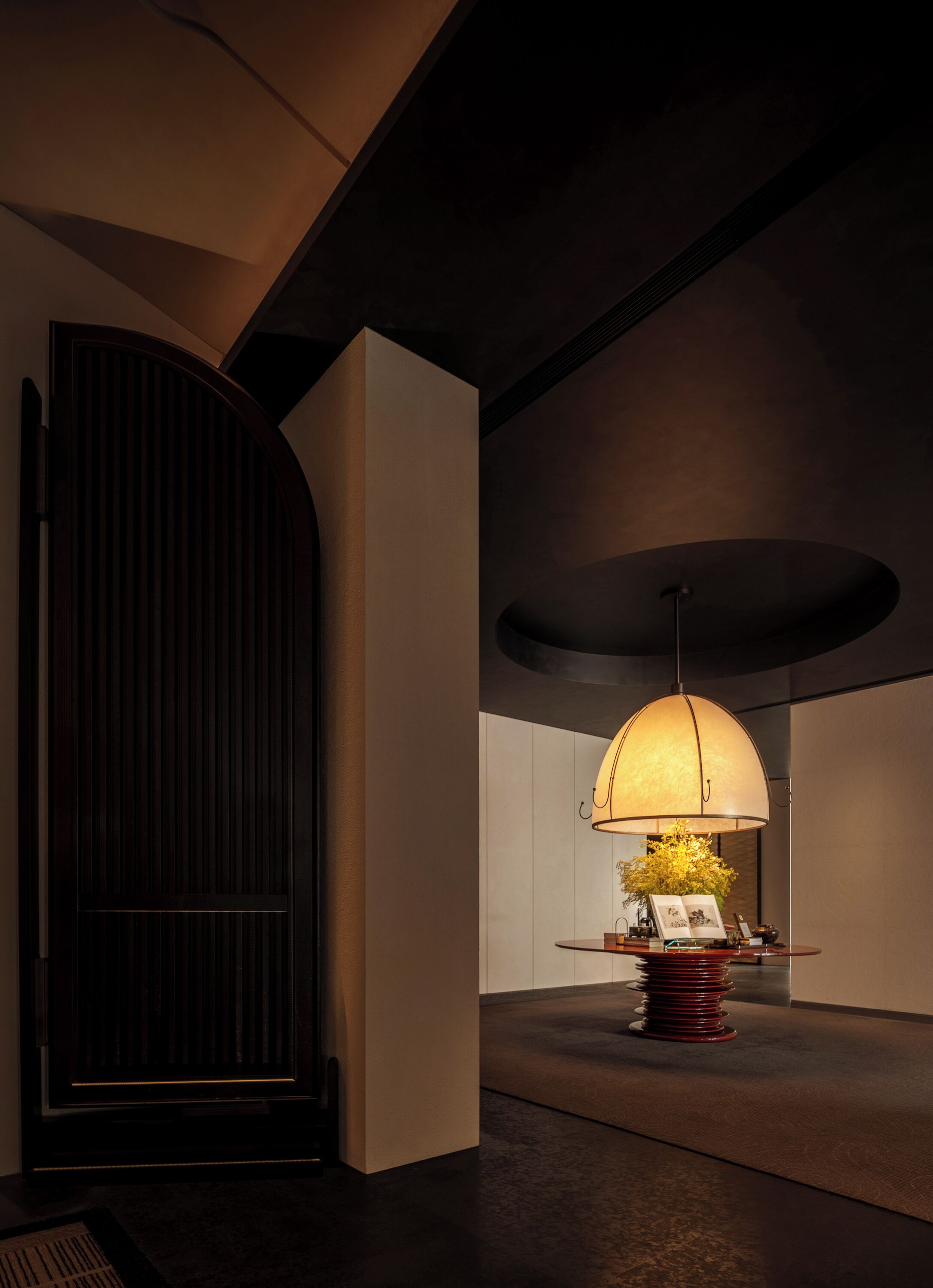 A modern interior with a large, dark wooden door, a round table with a lamp, and a minimalist design.
