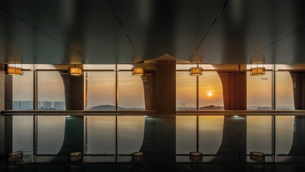 Une piscine intérieure moderne, dotée de grandes fenêtres qui reflètent le coucher de soleil et le paysage urbain.