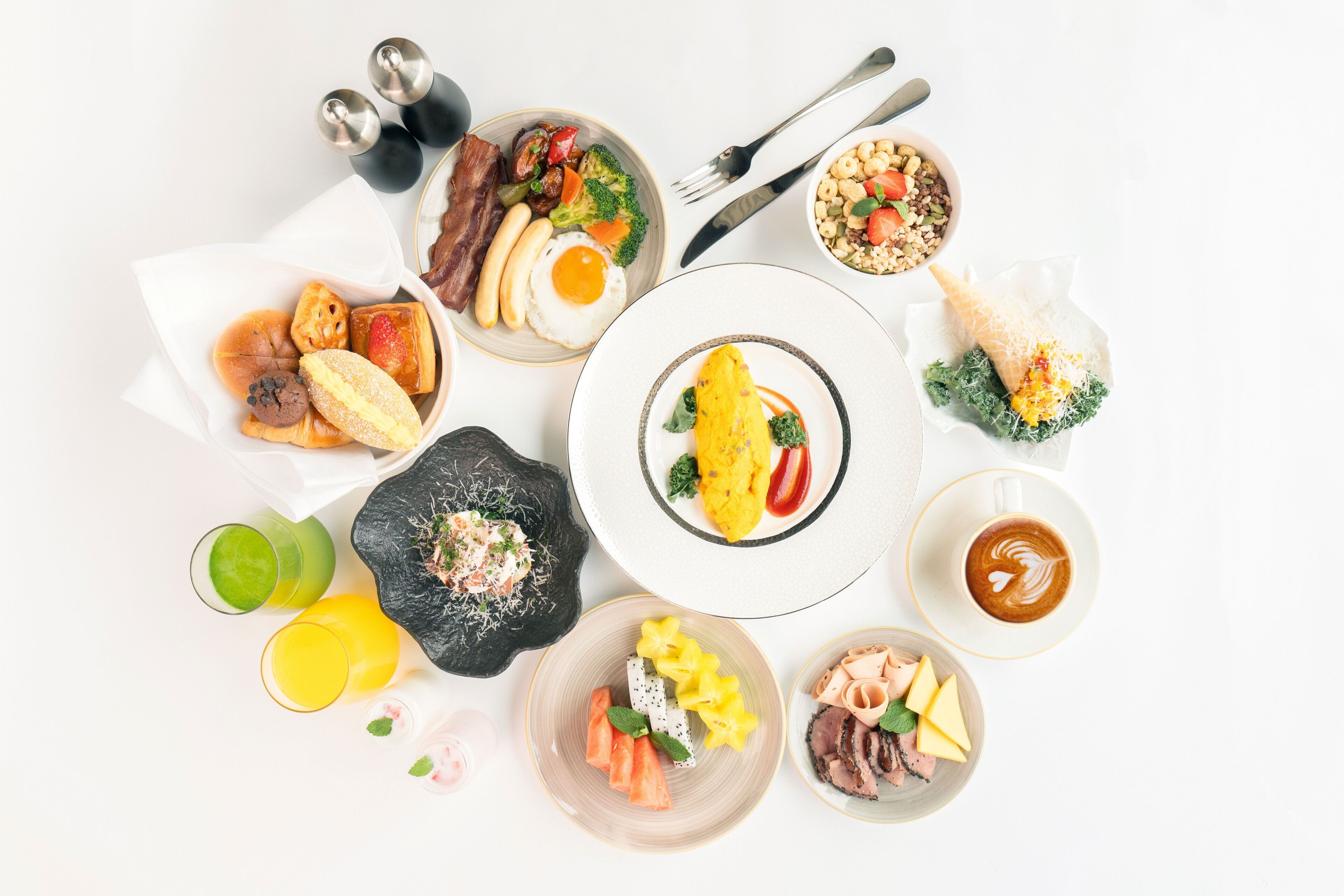 A variety of breakfast dishes including eggs, bacon, and fruits, arranged on a white table.