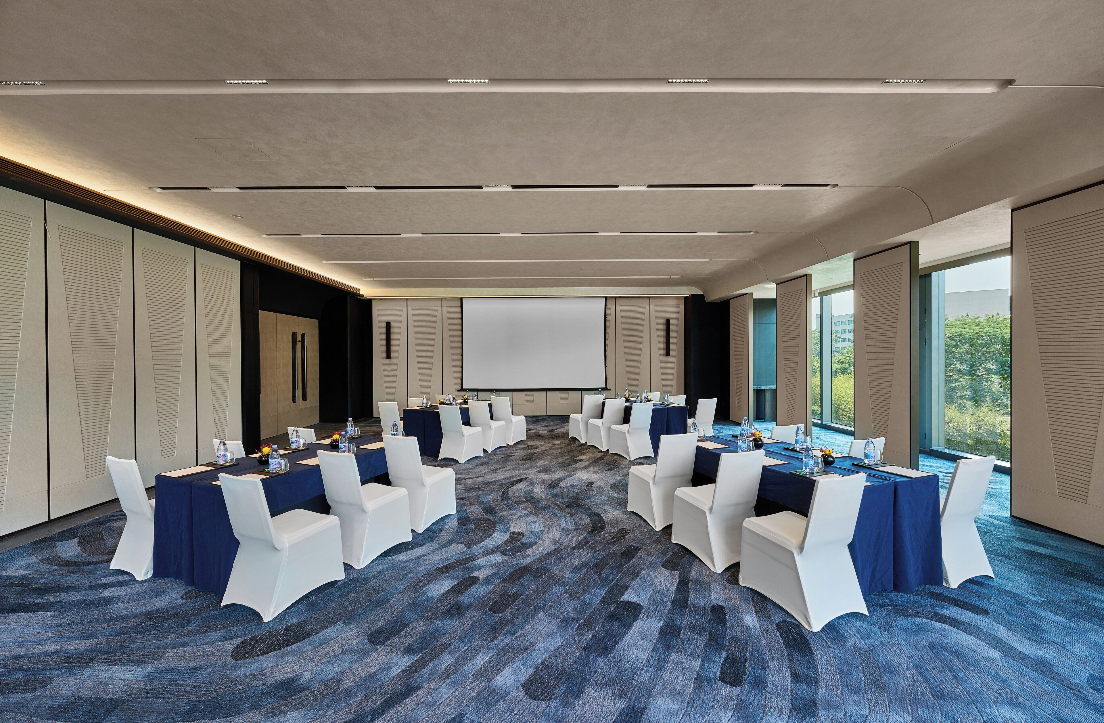 A conference room with a large screen, white chairs, and tables set up for a meeting.