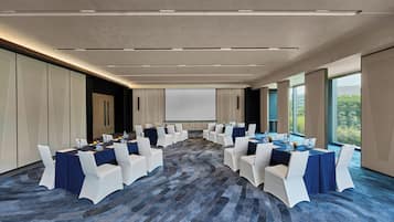 A conference room with a large screen, white chairs, and tables set up for a meeting.