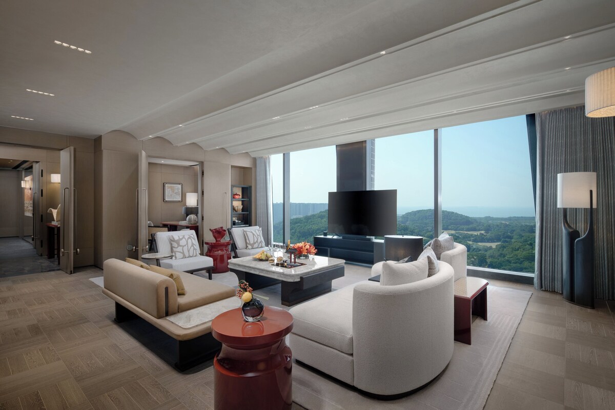 A modern living room with a large flat-screen TV, comfortable seating, and a view of the outdoors.