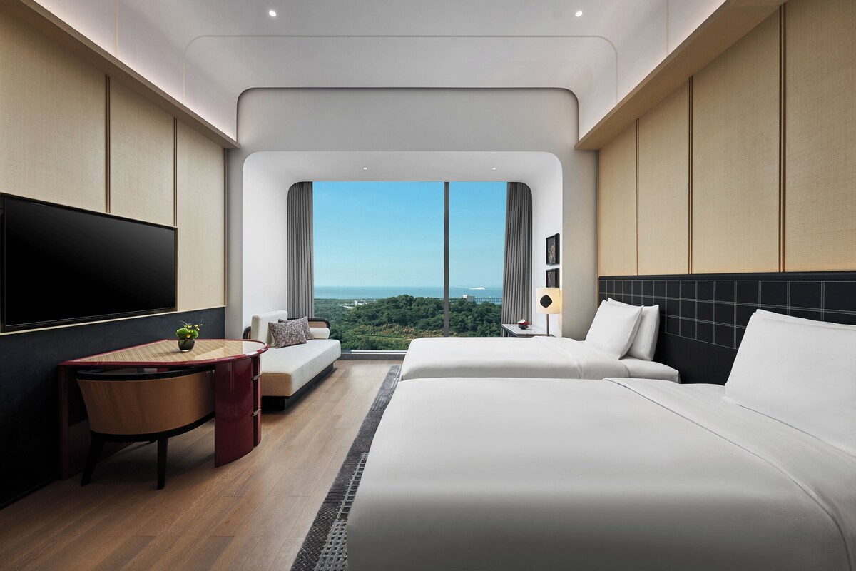 A modern hotel room with a large bed, a desk, a sofa, and a TV.