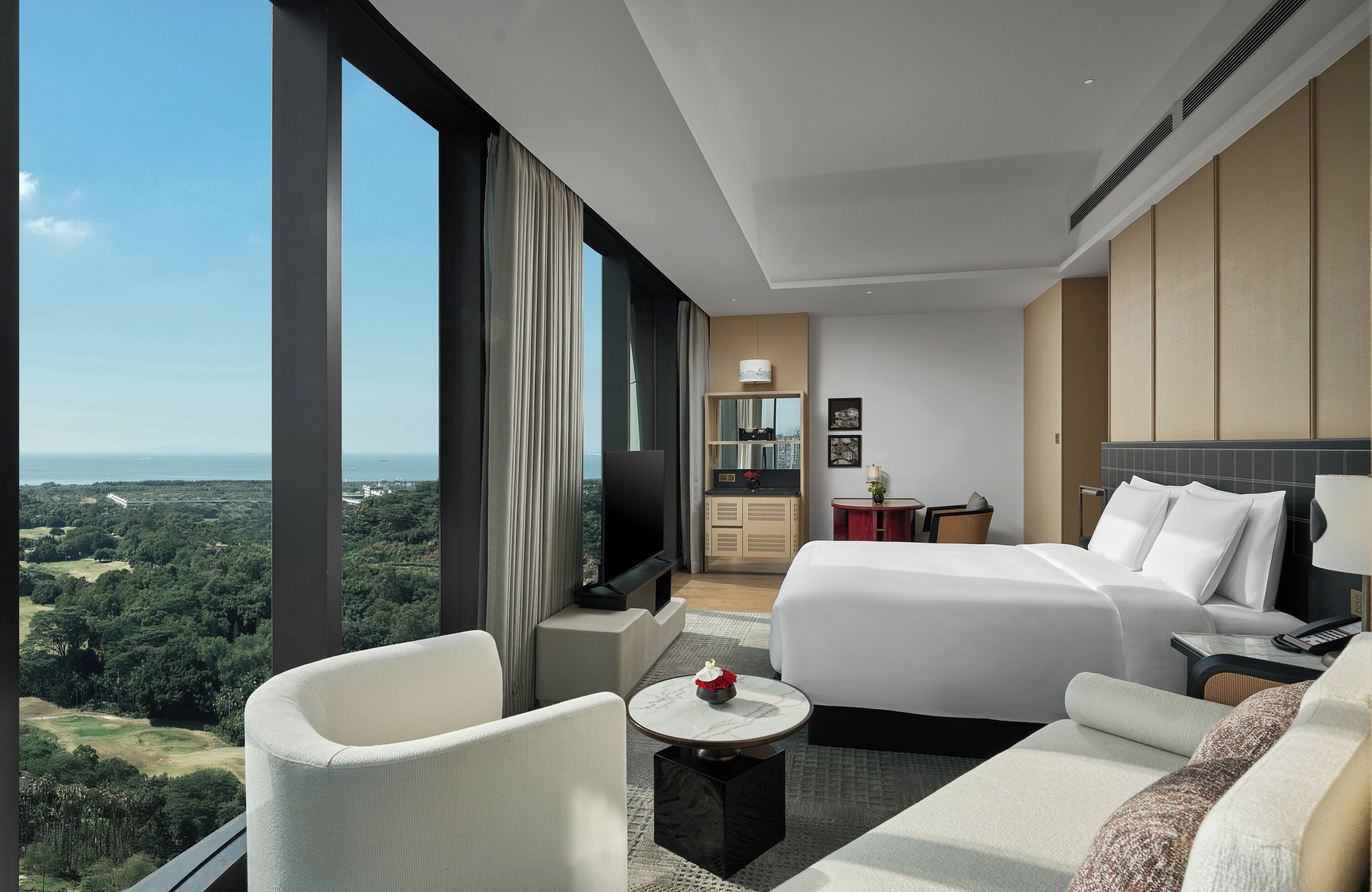 Ein Hotelzimmer mit einem großen Bett, einer Couch, einem Fernseher, einer kleinen Küchenzeile und Blick auf die Landschaft.
