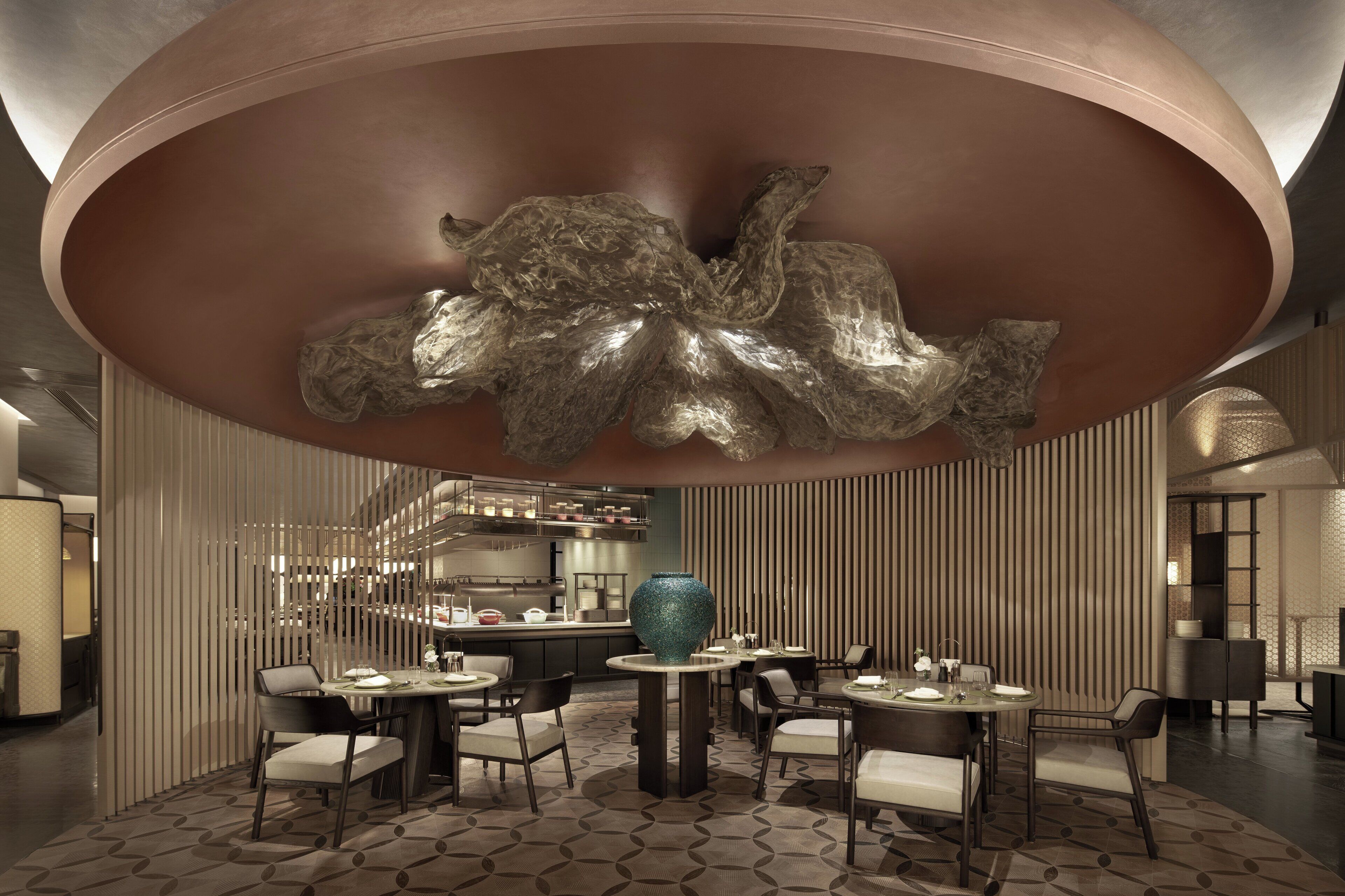 Uma área de jantar moderna com uma mesa central, rodeada por cadeiras, e uma escultura decorativa no teto.
