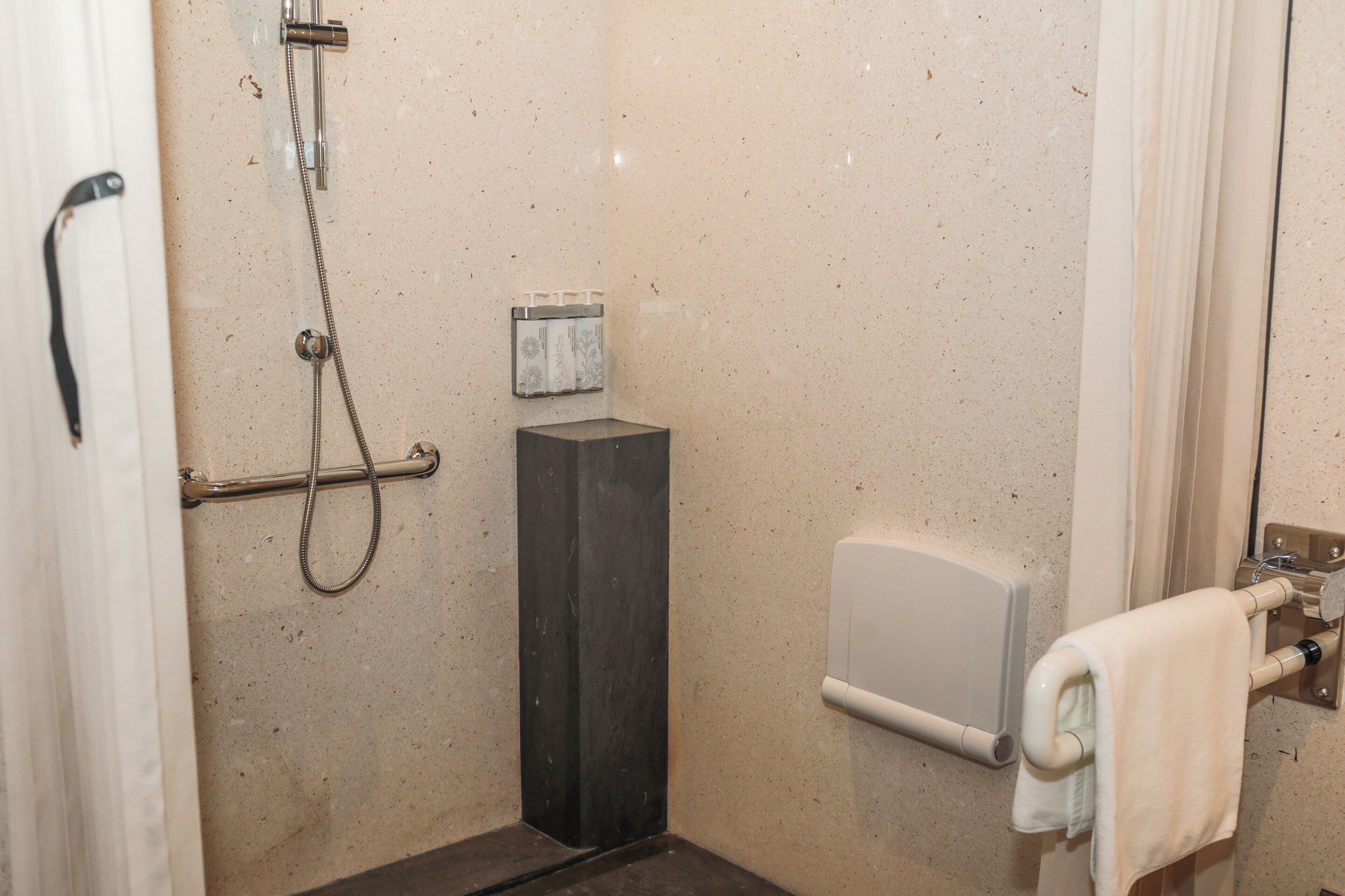 A small, enclosed shower area with a handheld showerhead, a towel dispenser, and a toilet paper holder.