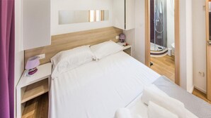 Una camera d'albergo con un letto, un comodino, uno specchio e un angolo doccia.
