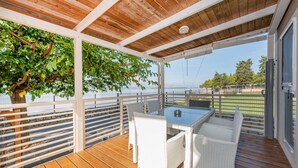 Un'area esterna riparata con un pavimento in legno, mobili in vimini bianco e vista sul mare.