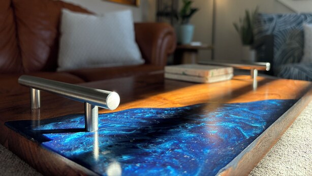 Een houten salontafel met een blauw sterrenstelsel ontwerp, een leren bank met een wit kussen, een klok en een vloerlamp in een woonkamer.