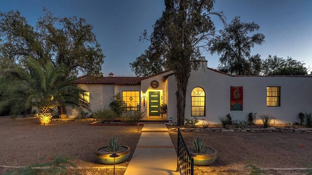 A two-story house with a stucco exterior, a front porch, and a well-lit entrance. - Casita Sam Hughes/University King bed (Tucson)
