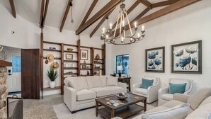 A spacious living room with a large sofa, a coffee table, and a chandelier. There are shelves with decorative items and framed artwork on the walls. - Pool & Hot tub! Sam Hughes University Lux!Walkable (Tucson)