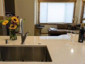 Una cucina con un lavandino in acciaio inossidabile, un vaso di girasoli e una bottiglia di vino sul bancone.