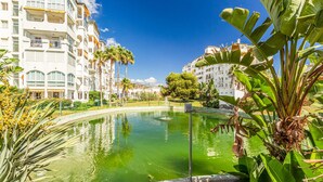 A pool surrounded by lush greenery and white buildings with balconies.