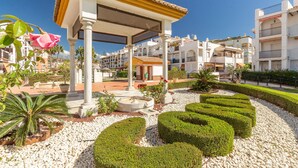 A courtyard with a pergola, white columns, a fountain, and neatly trimmed hedges.