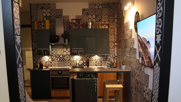 Una cucina moderna con zoccolo paraschizzi decorato, pavimento in legno e un’area bar con sgabelli.