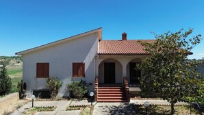 Une maison à deux étages, avec un toit recouvert de tuiles, un porche à l’avant avec des marches et un petit jardin.