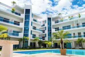 A modern multi-story hotel with a swimming pool, balconies, and tropical landscaping.