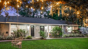 Une maison avec une pelouse bien entretenue, des guirlandes lumineuses suspendues et un fauteuil suspendu.