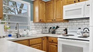 Une cuisine avec des meubles de rangement en bois, un micro-ondes blanc, une cuisinière et un évier.