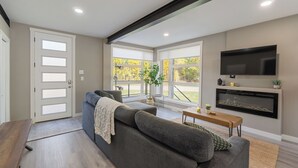 Een moderne woonkamer met een grijze bank, een houten salontafel, een open haard en een aan de muur bevestigde televisie.