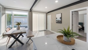 Een moderne woonkamer met een groot raam, een eethoek met een houten tafel en stoelen, en een witte bank.