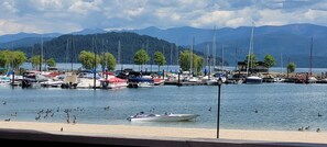 A marina with boats docked, a sandy beach, and mountains in the background.