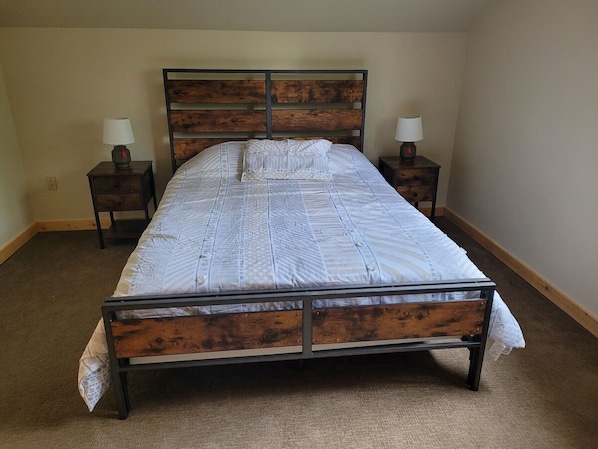 A single bed with a wooden frame and headboard, two bedside tables with lamps, and a carpeted floor.