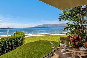 Une terrasse avec une table et des chaises, un arrangement floral et une vue sur l’océan.